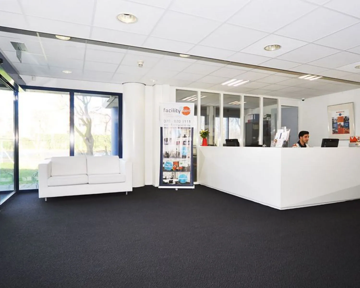 Moderne ontvangstruimte met een witte balie, een bank en grote ramen in een kantoor aan de Platinaweg 25 in Den Haag.