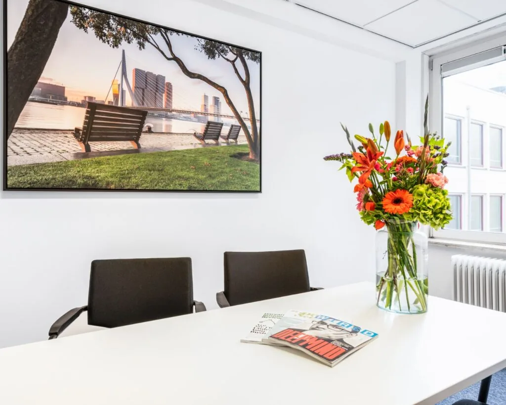 Moderne vergaderruimte aan de Posthoornstraat 17 in Rotterdam met bloemen op tafel en een foto van de Erasmusbrug aan de muur.