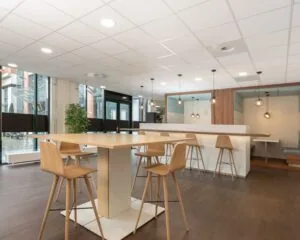 Moderne kantoorruimte aan het Stationsplein 91-105 in Den Bosch met hoge tafels, houten barkrukken en zithoeken met hanglampen.