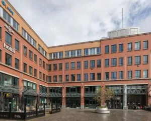 Bakstenen kantoorgebouw aan het Stationsplein 91-105 in Den Bosch met zicht op diverse bedrijfsnaamborden en een glazen entree.