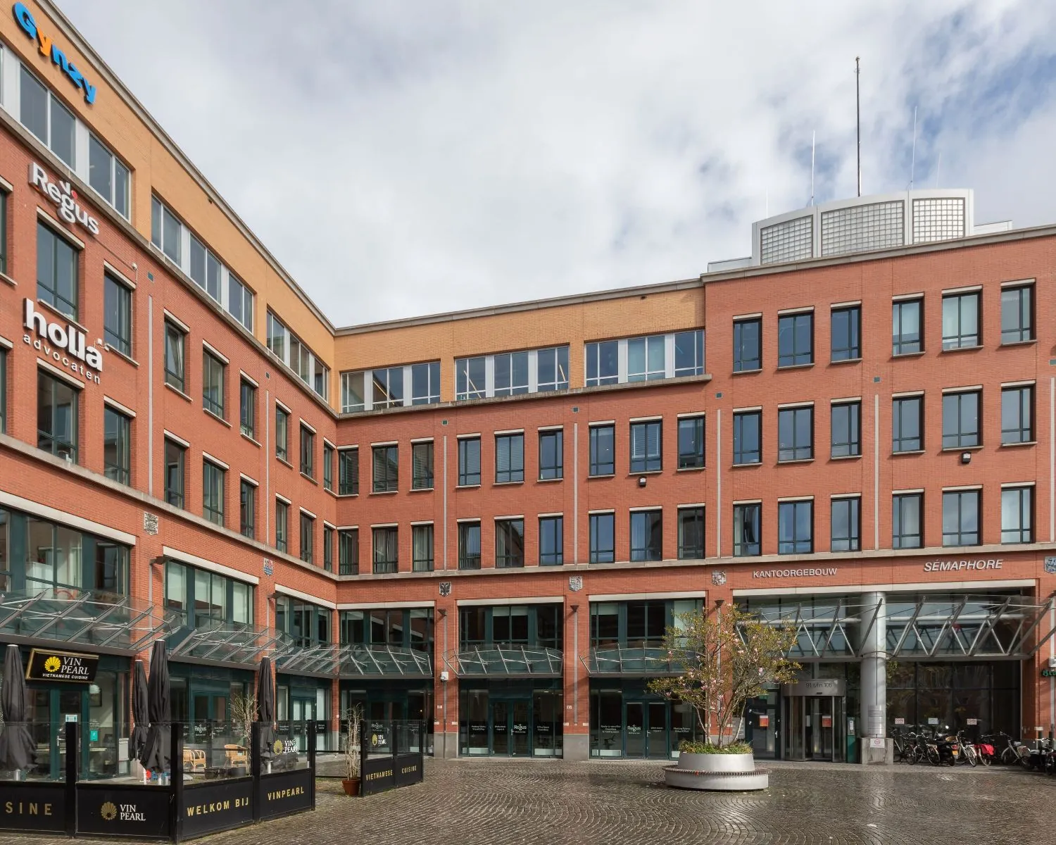 Bakstenen kantoorgebouw aan het Stationsplein 91-105 in Den Bosch met zicht op diverse bedrijfsnaamborden en een glazen entree.
