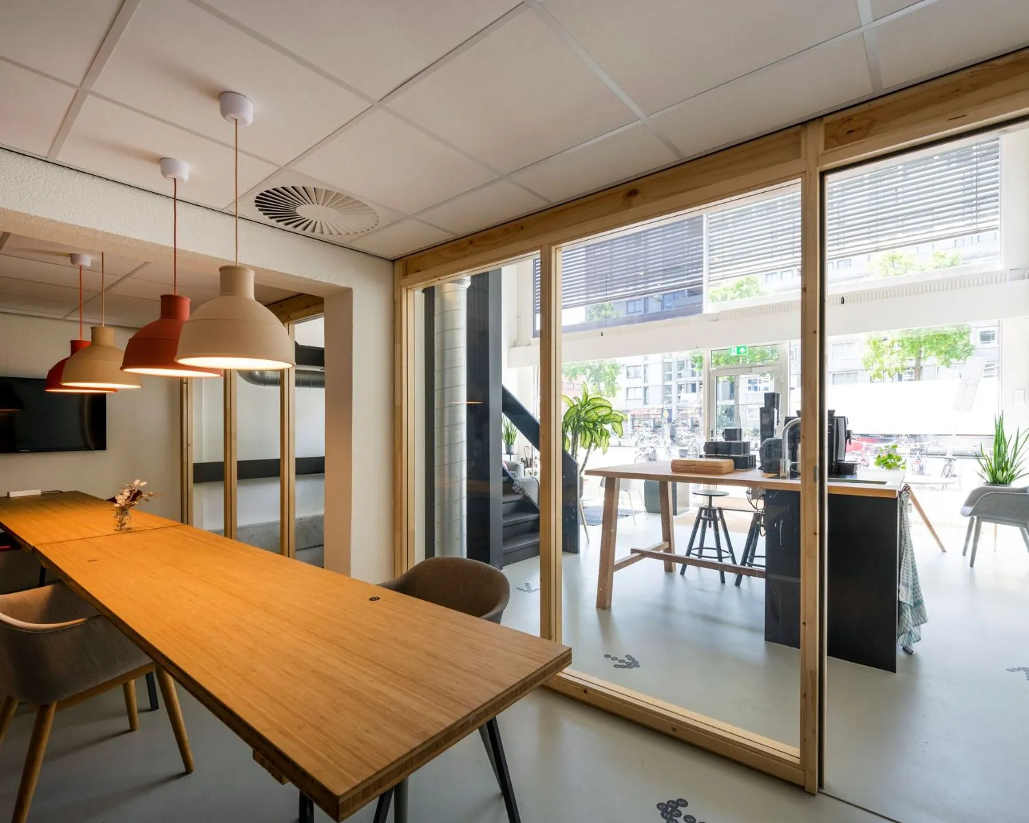 Moderne kantoorruimte aan de Weesperstraat 61 in Amsterdam met houten vergadertafel, hanglampen en glazen wand met zicht op werkplekken en straatzicht.