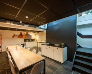 Moderne kantoorkeuken met lange houten eettafel, designlampen en trap bij Weesperstraat 61 in Amsterdam.