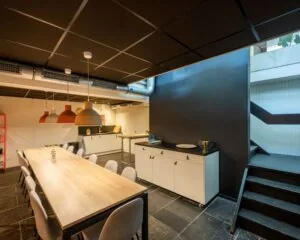 Moderne kantoorkeuken met lange houten eettafel, designlampen en trap bij Weesperstraat 61 in Amsterdam.