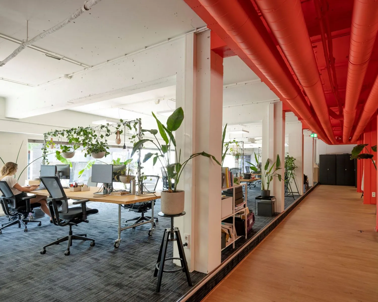 Moderne kantoorruimte aan de Weesperstraat 61 in Amsterdam met open werkplekken, veel planten en opvallende rode plafondbuizen.