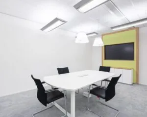 Moderne vergaderruimte met witte tafel, vier zwarte stoelen en een groot scherm aan de muur in kantoor Willemsplein 2, Den Bosch.