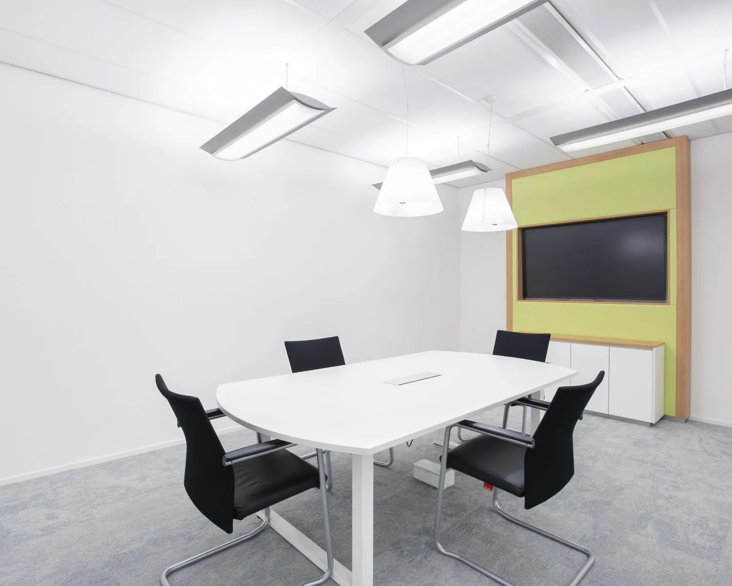 Moderne vergaderruimte met witte tafel, vier zwarte stoelen en een groot scherm aan de muur in kantoor Willemsplein 2, Den Bosch.