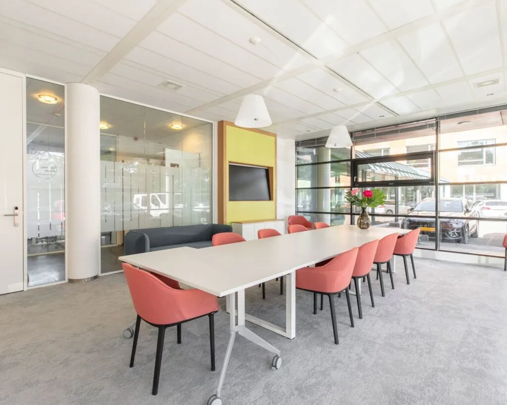 Moderne vergaderruimte met roze stoelen, een lange tafel en grote ramen aan de Databankweg 26 in Amersfoort.