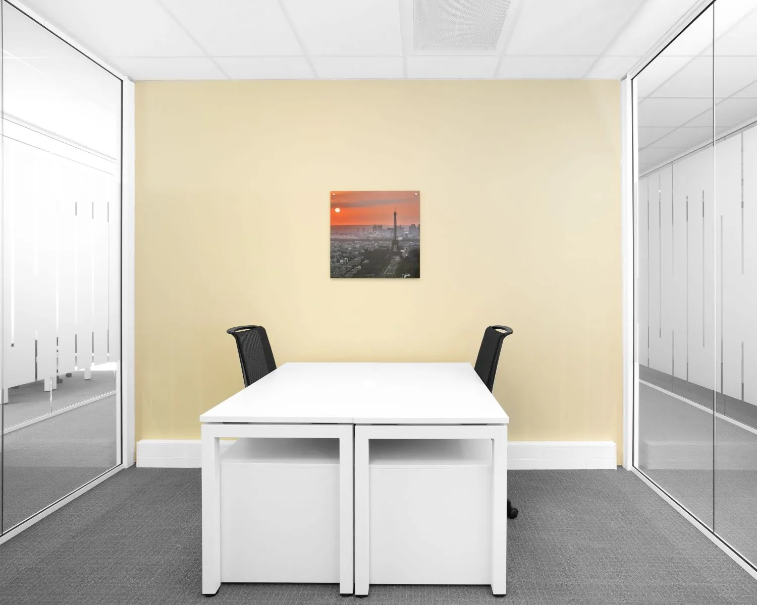 Moderne kantoorruimte in de Queenstower aan de Delflandlaan in Amsterdam met twee bureaus, glazen wanden en een foto van de Eiffeltoren aan de muur.