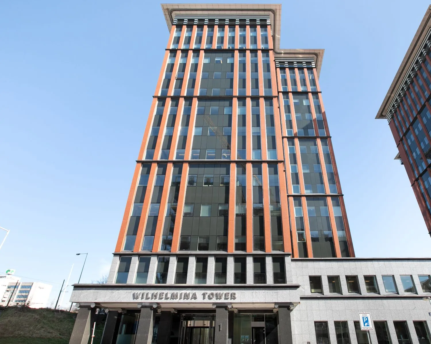 Voorgevel van de Wilhelmina Tower, een moderne kantoortoren aan de Delflandlaan in Amsterdam, onder een heldere blauwe lucht.