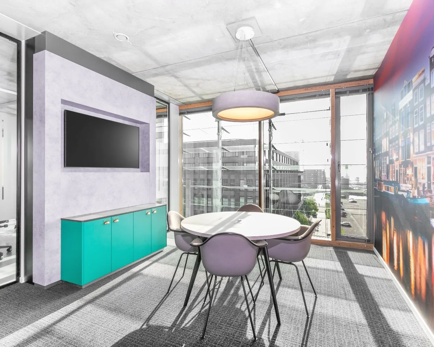 Moderne vergaderruimte in een kantoor aan de Kraanspoor 50 in Amsterdam met grote ramen, een ronde tafel, paarse stoelen en een wandfoto van Amsterdamse grachtenpandjes.
