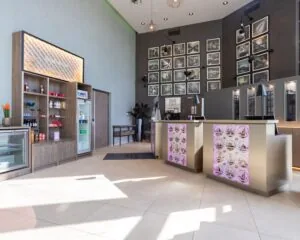 Moderne lobby van het Leonardo Royal Hotel in Amsterdam met receptiebalies, kunst aan de muur en een verkoophoek met snacks en drankjes.