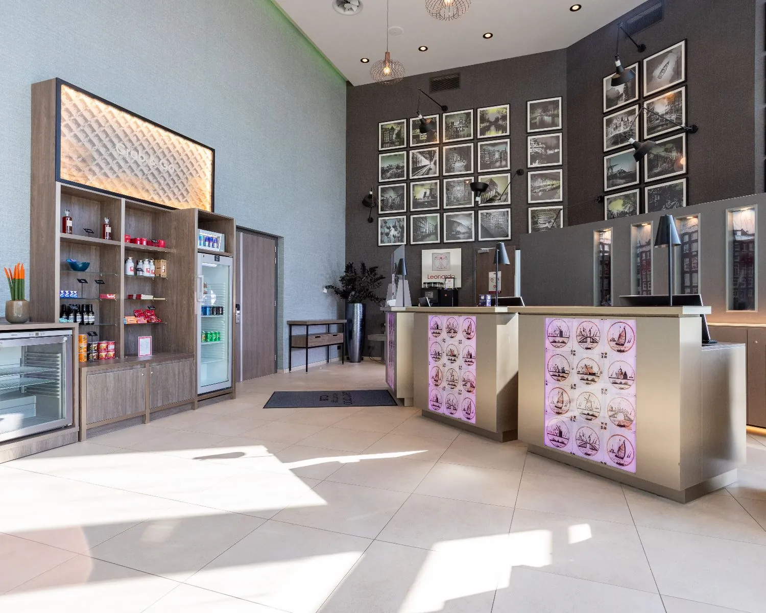 Moderne lobby van het Leonardo Royal Hotel in Amsterdam met receptiebalies, kunst aan de muur en een verkoophoek met snacks en drankjes.