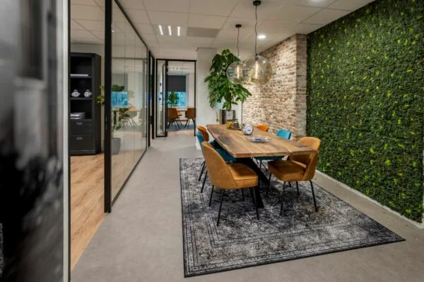Moderne vergaderruimte in Amsterdam met houten tafel, designstoelen, groene mossenwand en bakstenen muur.