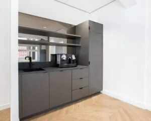 Moderne kantoorpantry met grijze kasten, zwarte kraan en een koffiezetapparaat in een kantoorruimte aan het Rokin in Amsterdam.