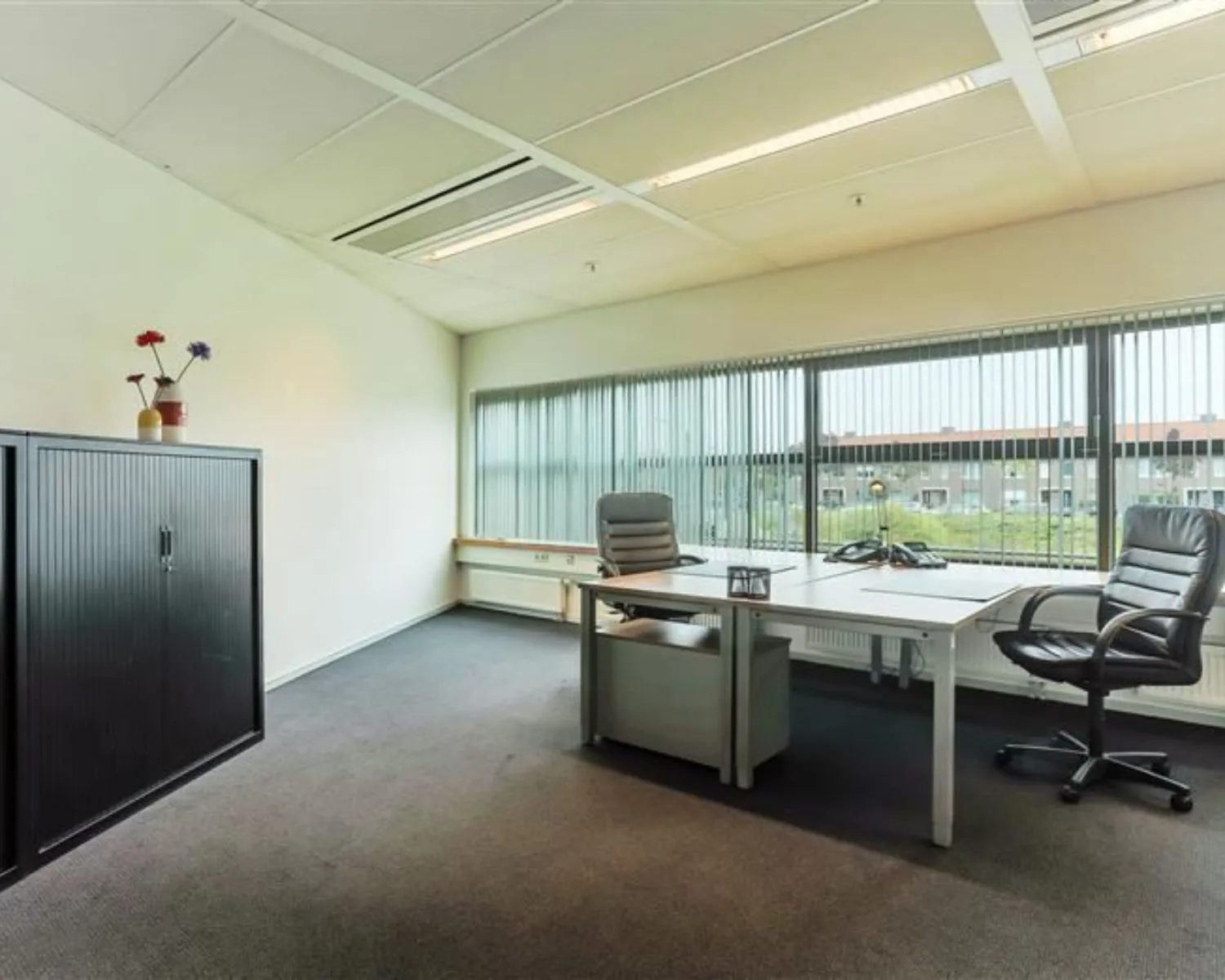 Moderne kantoorruimte te huur aan de Avenue Céramique 221 met twee bureaustoelen, groot raam en opbergkast.