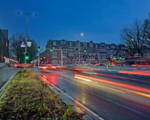 Drukke kruising bij de Benoordenhoutseweg in Den Haag met lichtsporen van voorbijrijdend verkeer in de avondschemering.