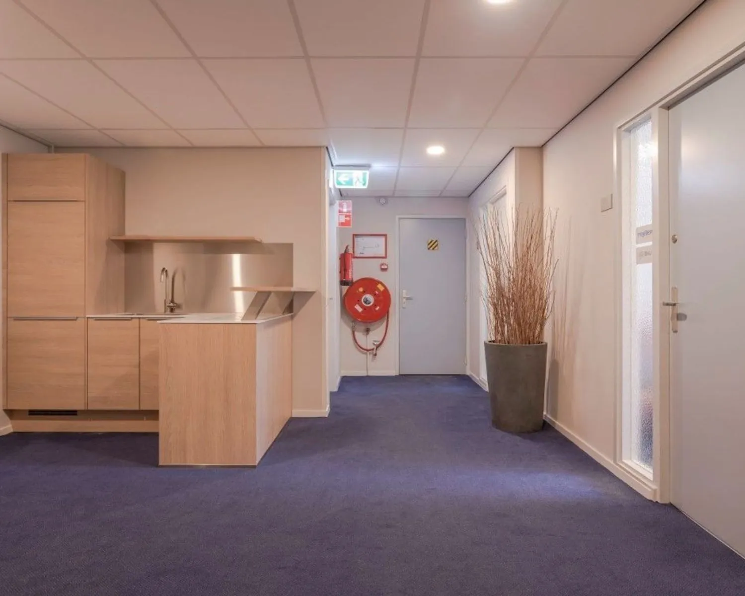 Moderne kantoorruimte aan de Benoordenhoutseweg met pantry, brandhaspel en blauwe vloerbedekking.