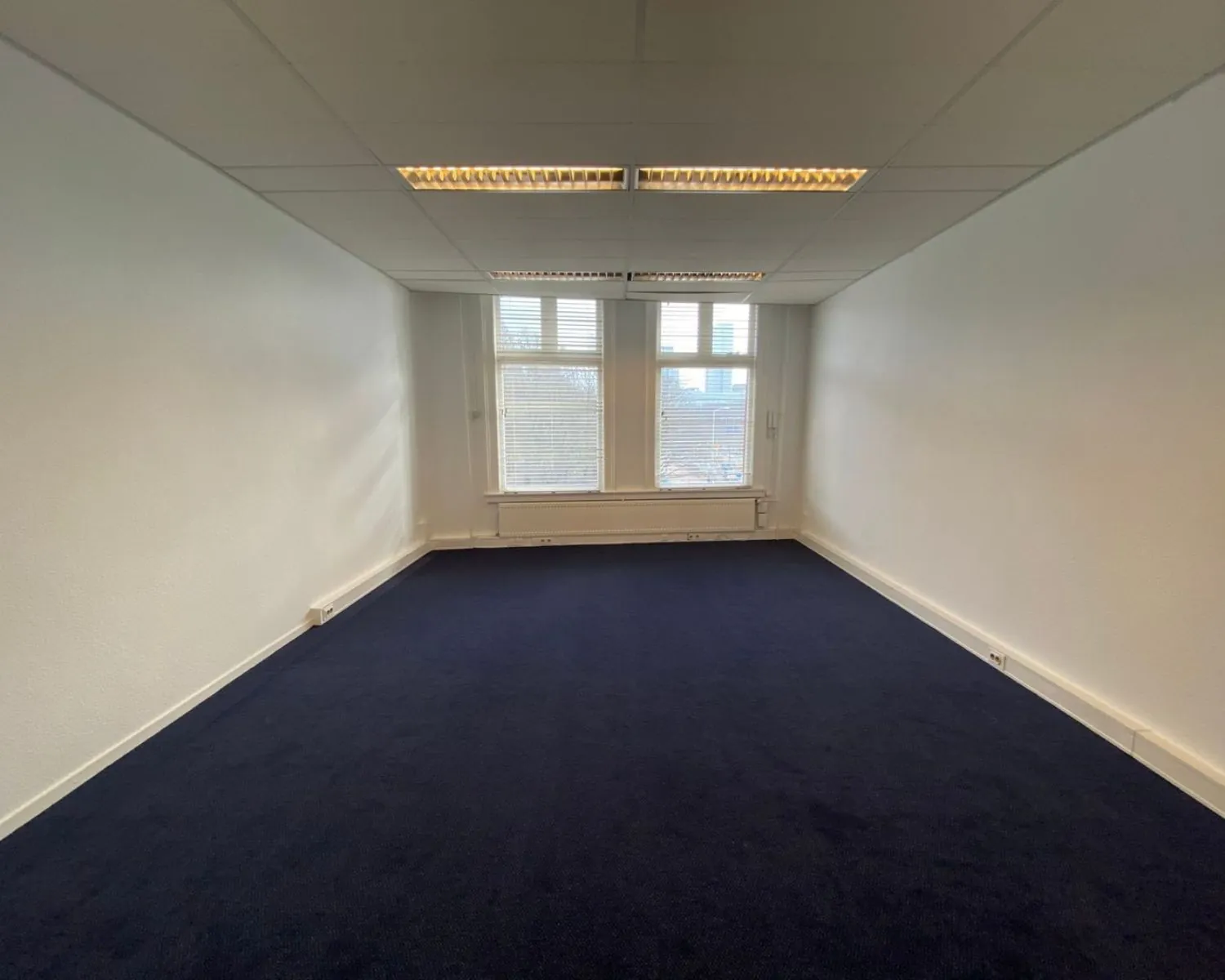 Leegstaande kantoorruimte met donkerblauwe vloerbedekking aan de Benoordenhoutseweg 21.