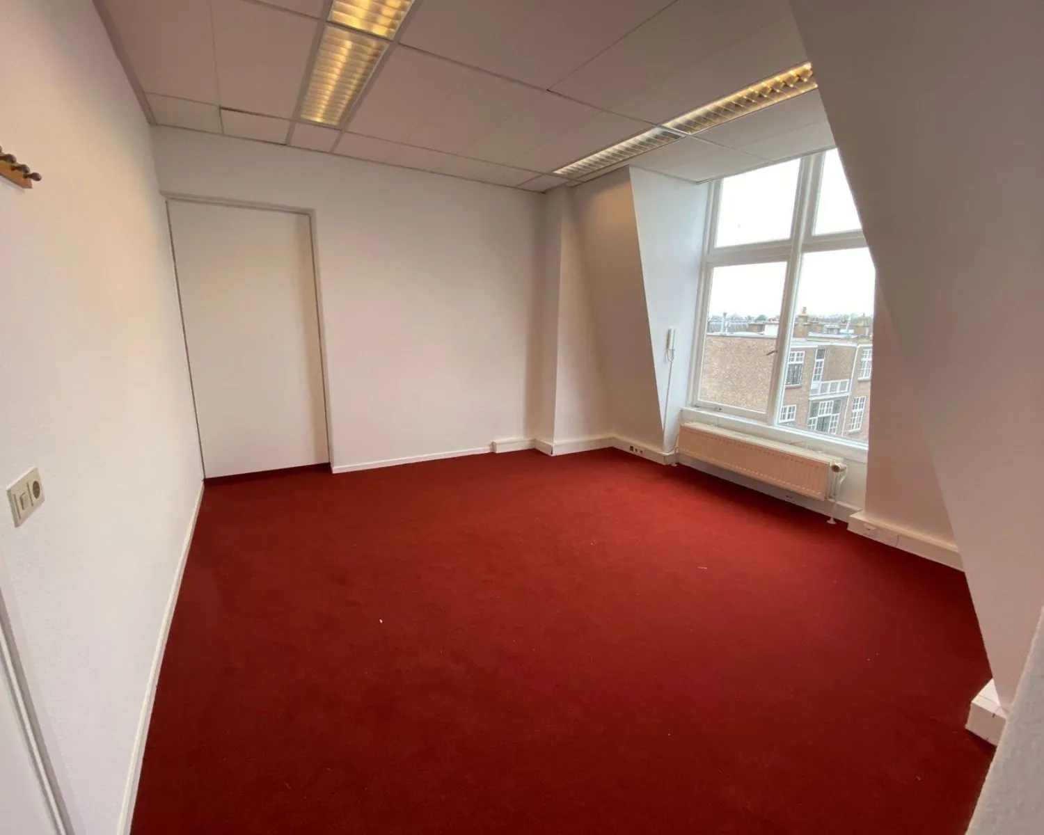 Lichte kantoorruimte met rood tapijt en groot raam aan de Benoordenhoutseweg 21.