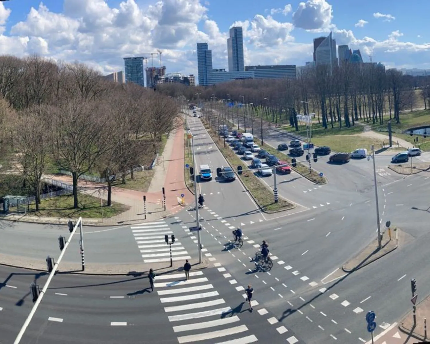 Drukke kruising op de Benoordenhoutseweg in Den Haag met uitzicht op kantoorgebouwen en het Haagse Bos.