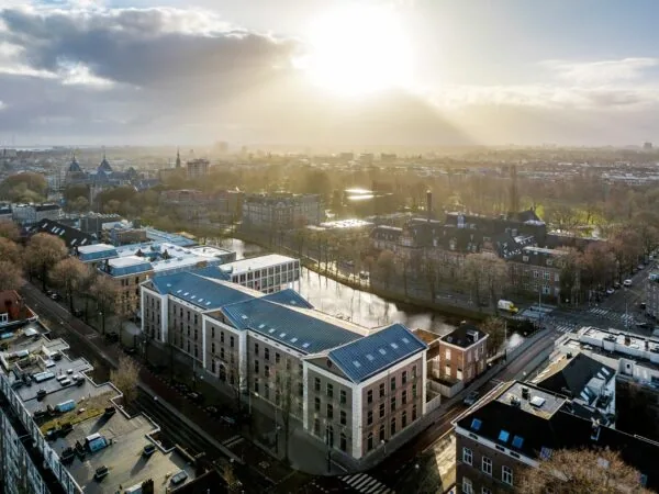 Luchtfoto van het kantoorgebouw De Bell aan de Sarphatistraat 370 in Amsterdam, bij zonsopkomst met uitzicht op de stad en omliggende grachten.