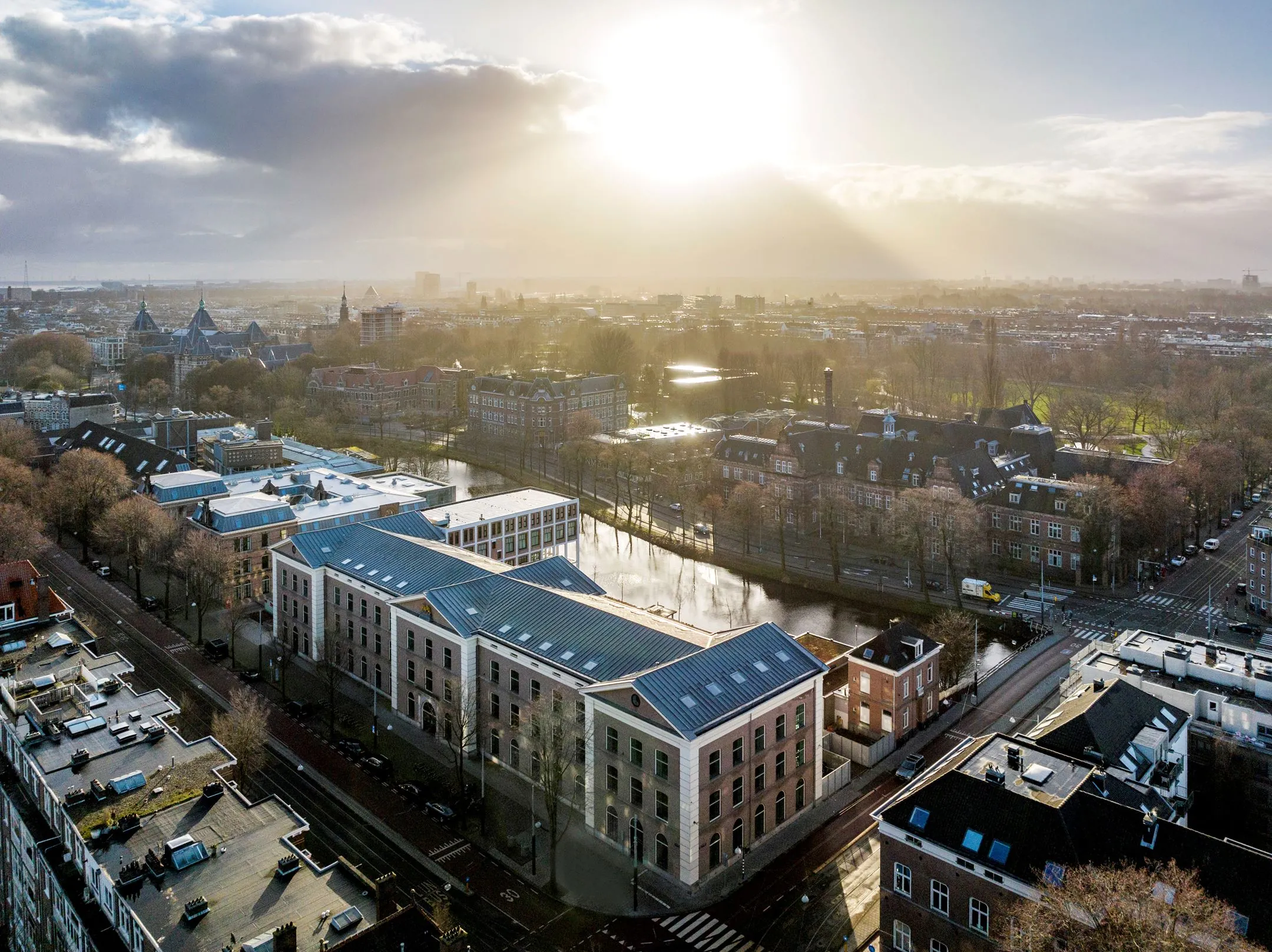 Luchtfoto van het kantoorgebouw De Bell aan de Sarphatistraat 370 in Amsterdam, bij zonsopkomst met uitzicht op de stad en omliggende grachten.