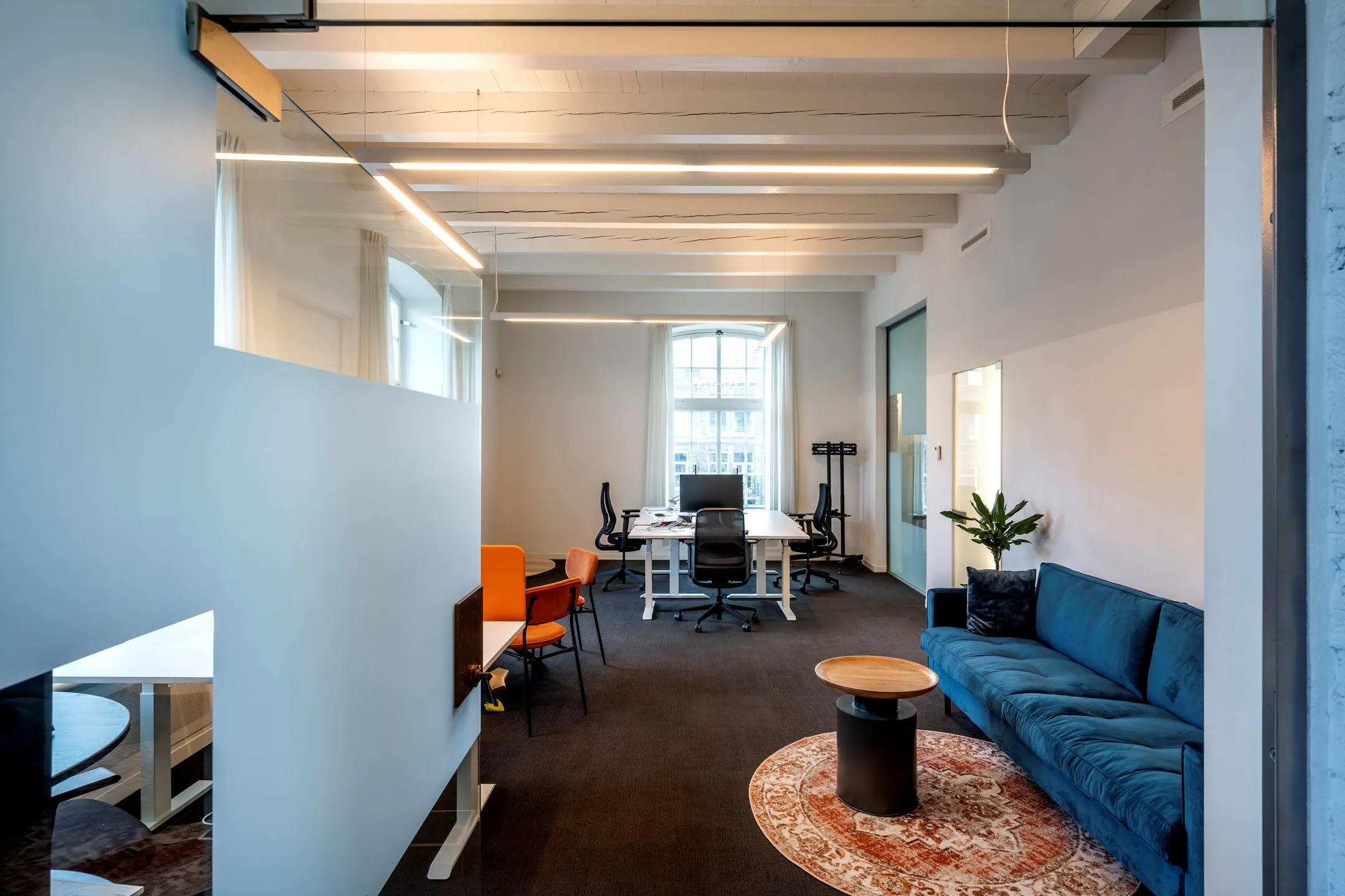 Moderne kantoorruimte te huur aan de Sarphatistraat 370 met werkplekken, vergadertafel, blauwe bank en grote ramen.