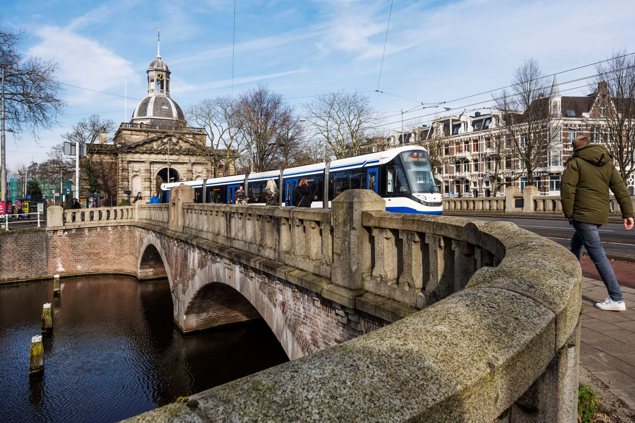 Tram op brug bij De Bell aan de Sarphatistraat 370 in Amsterdam met monumentale gebouwen op de achtergrond.