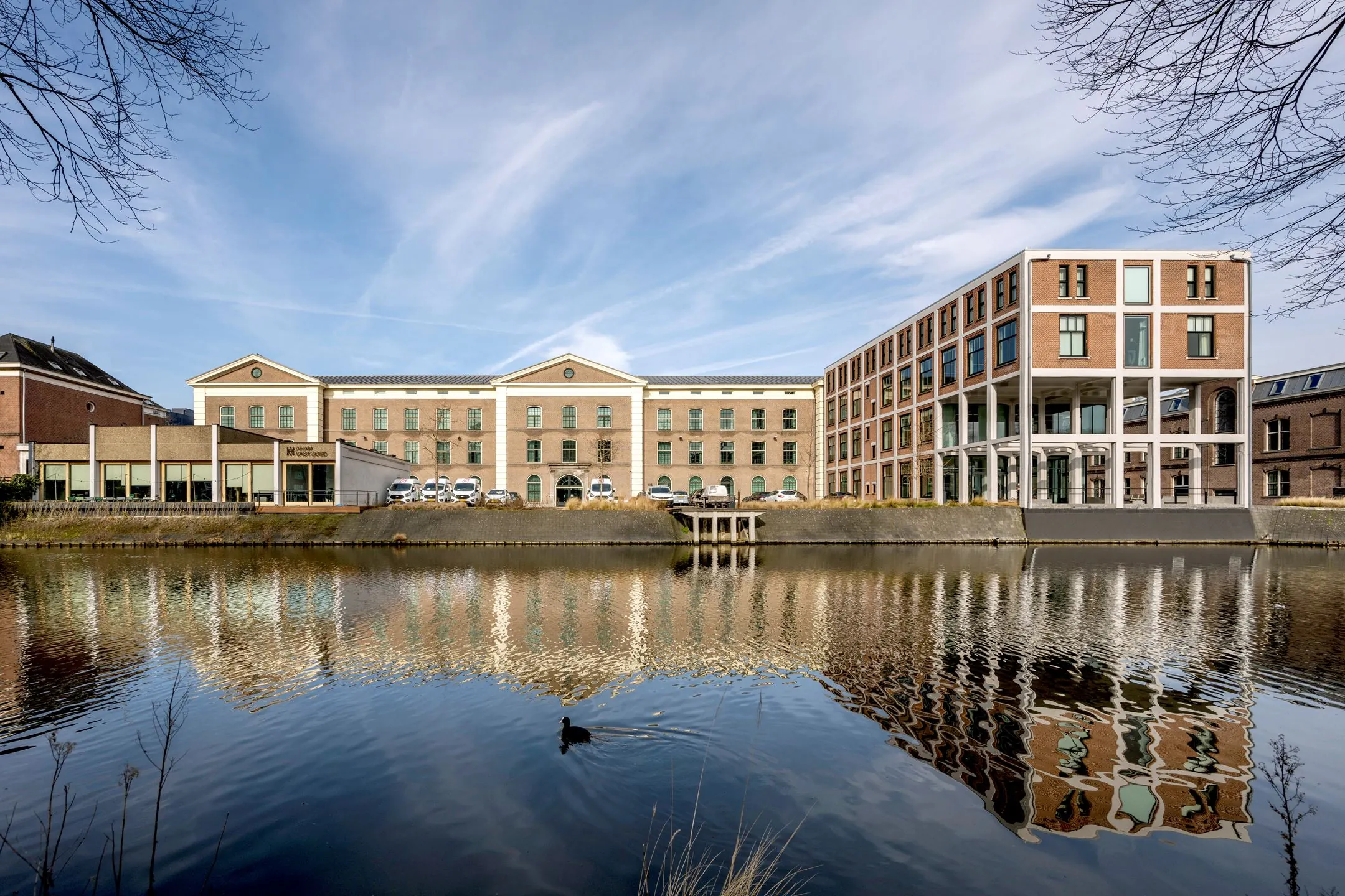 Vooraanzicht van kantoorverzamelgebouw De Bell aan de Sarphatistraat 370-22 in Amsterdam, met weerspiegeling in het water.