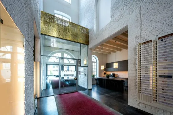 Entreehal van kantoorruimte De Bell aan de Sarphatistraat 370 met hoge plafonds, moderne receptie en bedrijfsnaambord.