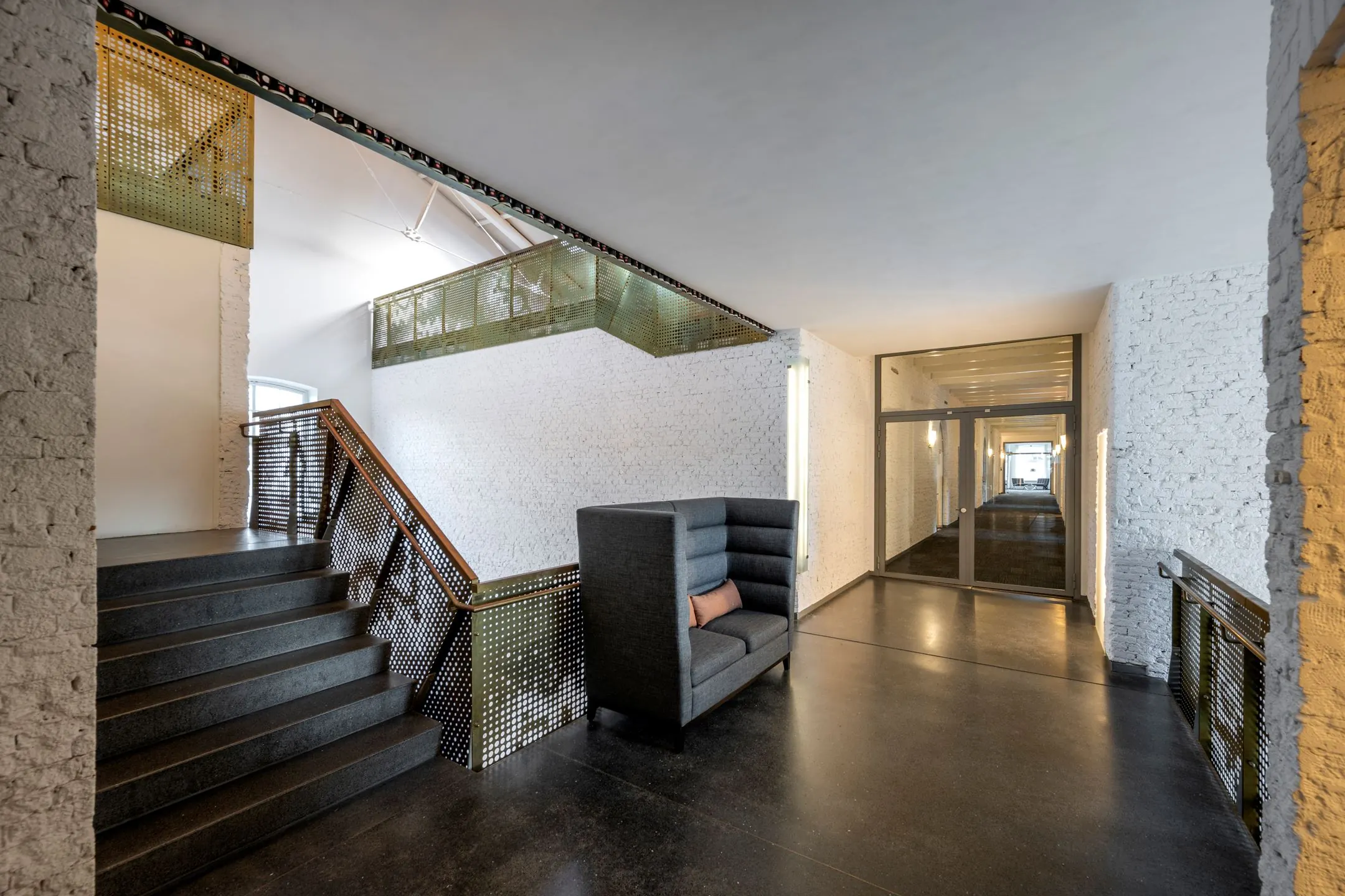 Moderne kantoorruimte in De Bell aan de Sarphatistraat 370 met loungestoel, trap en gang met glazen deur.