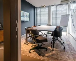 Moderne vergaderruimte met zes stoelen, een flatscreen, flip-over en grote ramen aan de President Kennedylaan 19 in Den Haag.