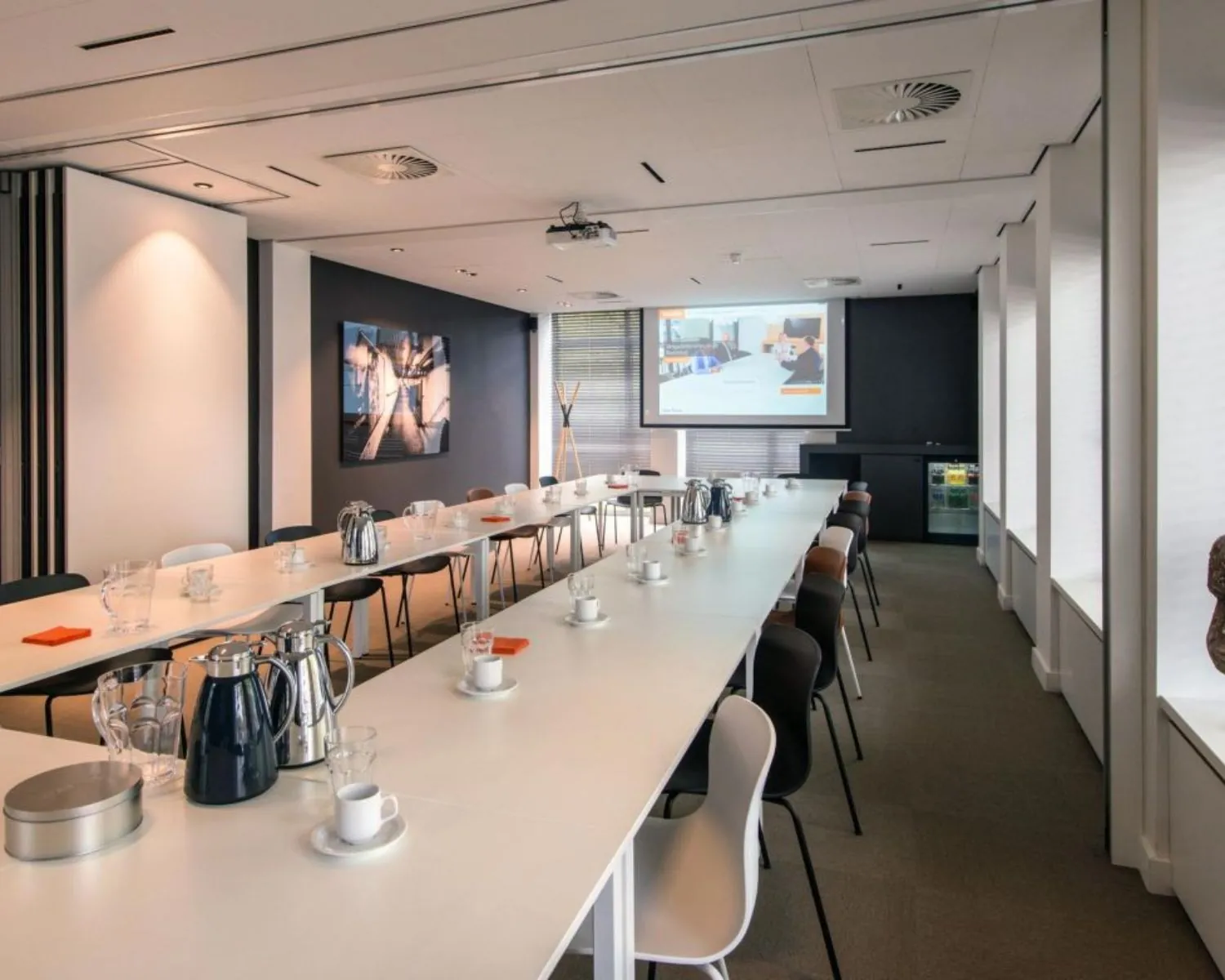 Moderne vergaderruimte met lange tafels, presentatiescherm en koffievoorzieningen aan de President Kennedylaan 19 in Den Haag.