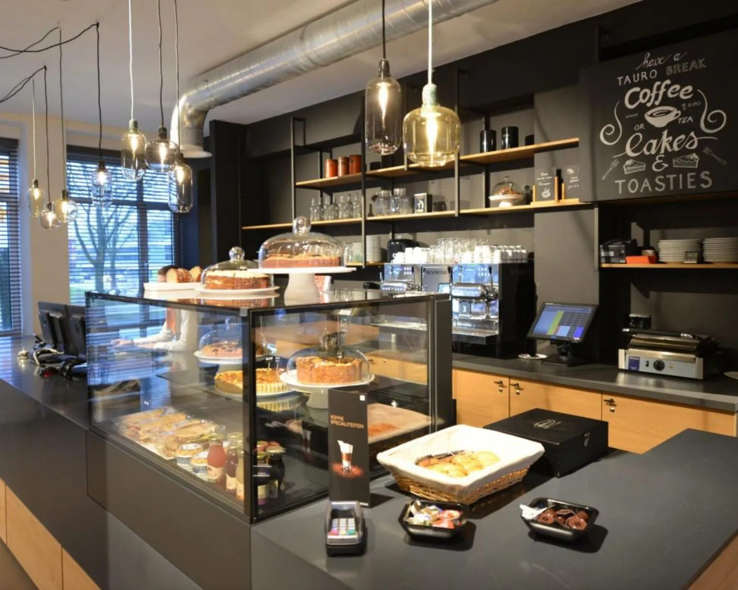 Moderne koffiecorner met vitrine vol gebak en broodjes in een kantoorgebouw aan de President Kennedylaan 19 in Den Haag.