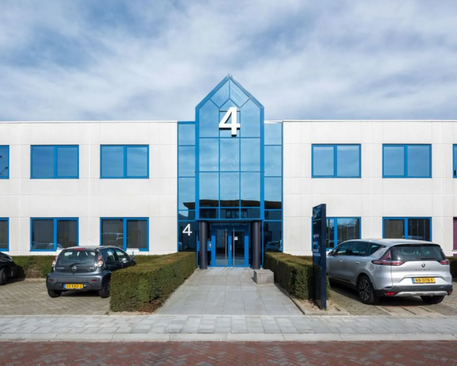Vooraanzicht van een modern kantoorgebouw aan de Europalaan 4 in Den Bosch, met parkeerplaatsen en blauwe kozijnen.
