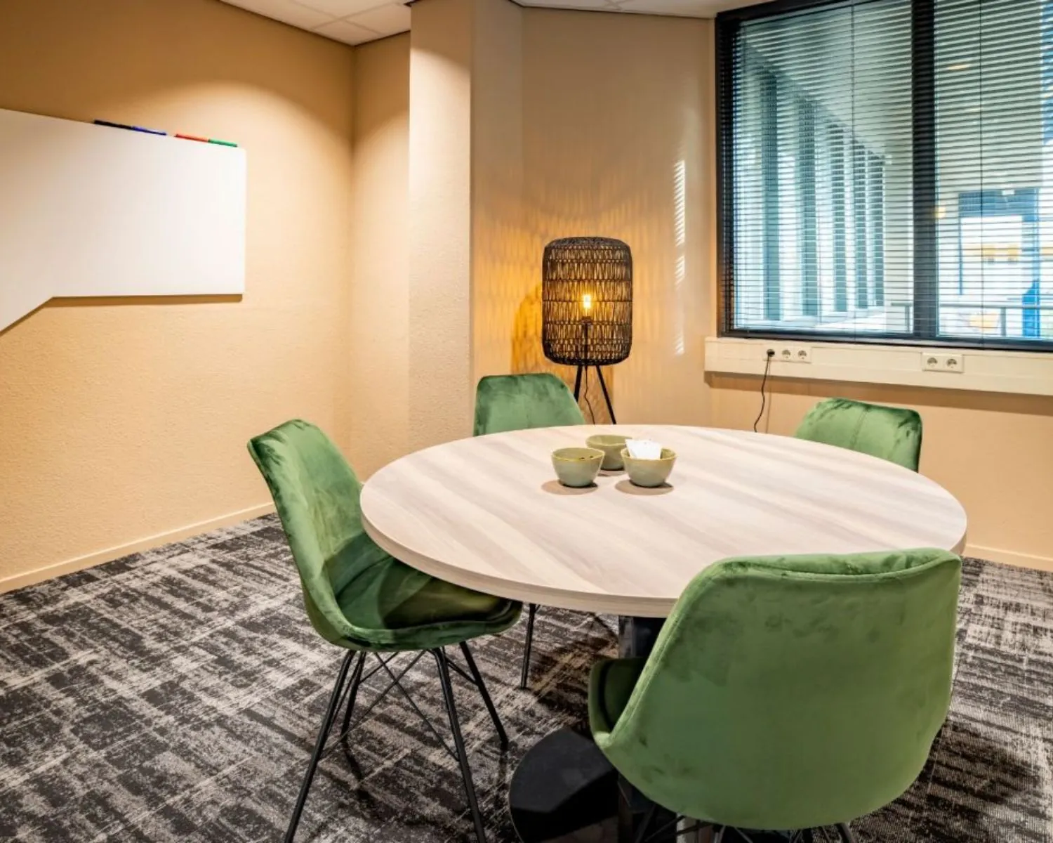 Moderne kantoorruimte aan de Europalaan in Den Bosch met ronde vergadertafel, groene stoelen en een sfeervolle lamp.
