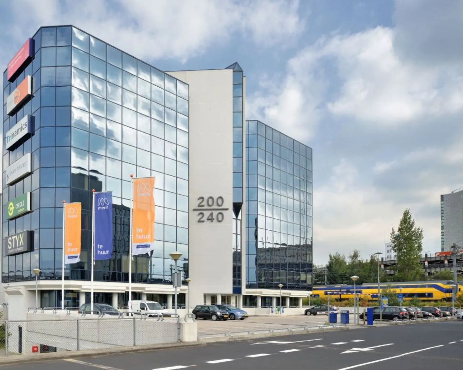 Glazen kantoorgebouw aan Fellenoord 200-240 in Eindhoven met te huur-banners en zicht op een voorbijrijdende NS-trein.