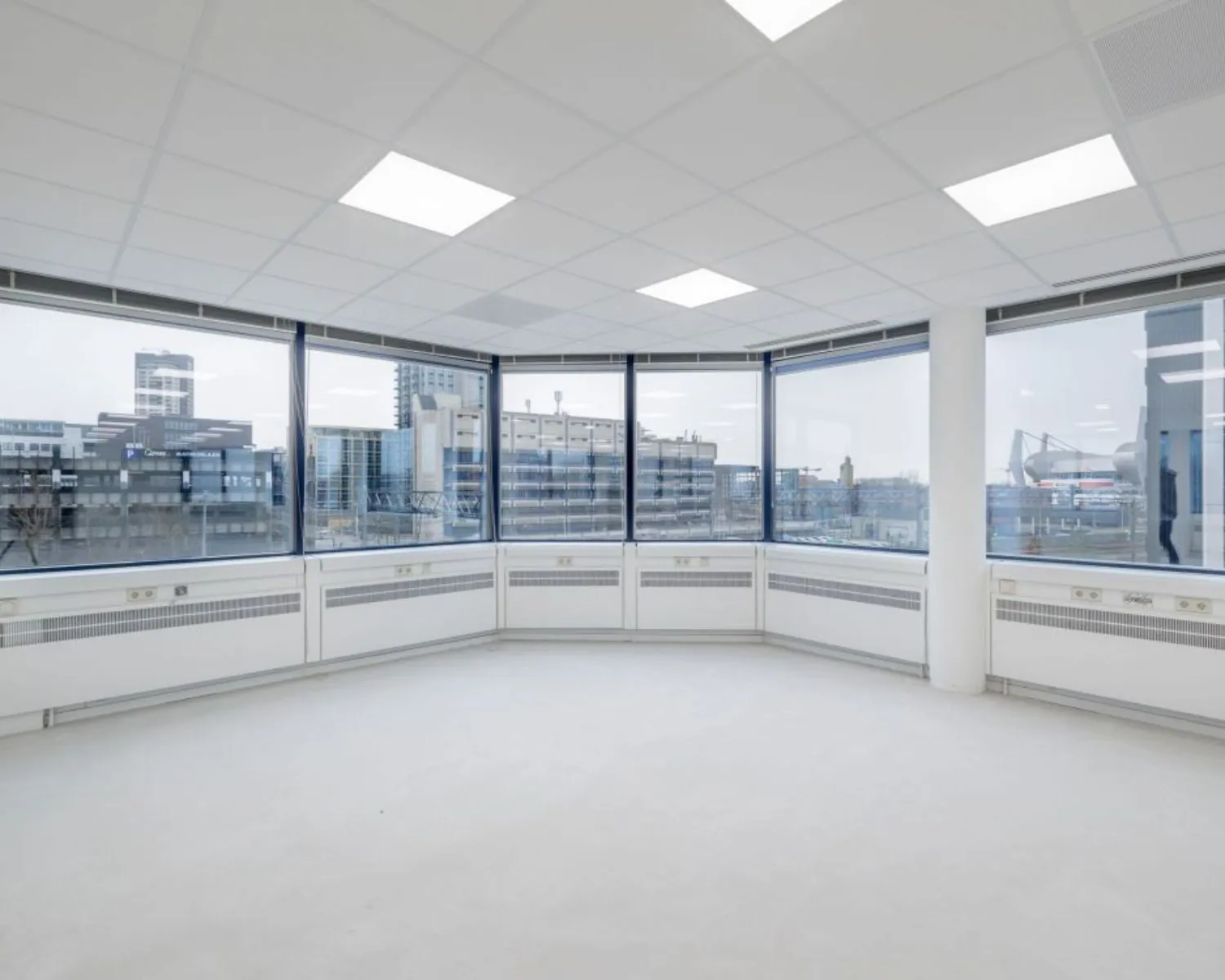 Lichte, lege kantoorruimte met grote ramen en uitzicht op de gebouwen aan de Fellenoord in Eindhoven.