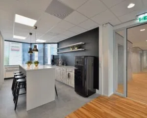 Moderne keukenhoek in kantoorruimte aan Fellenoord 200-240 in Eindhoven met hoge tafel, barkrukken en zwarte SMEG-koelkast.