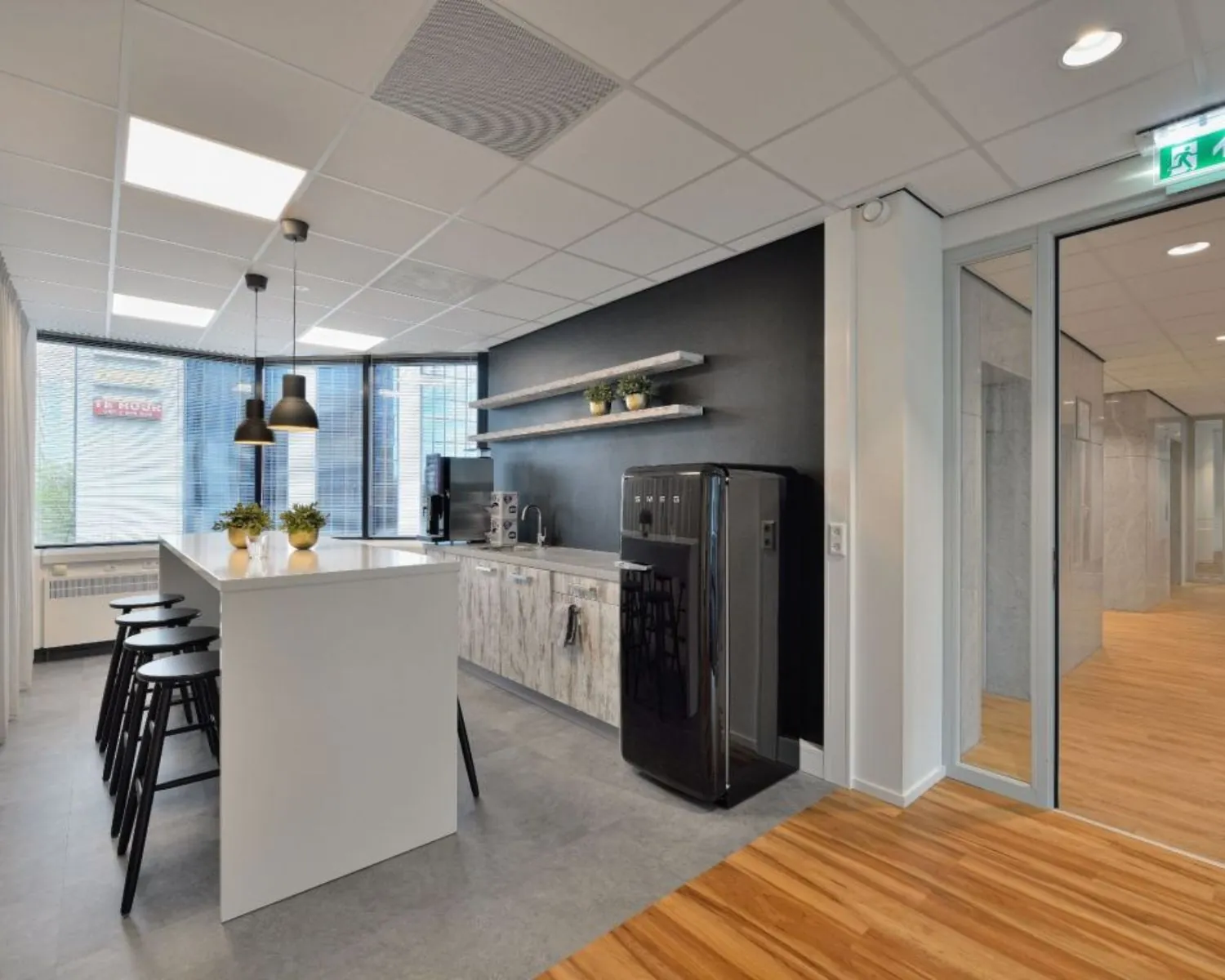 Moderne keukenhoek in kantoorruimte aan Fellenoord 200-240 in Eindhoven met hoge tafel, barkrukken en zwarte SMEG-koelkast.