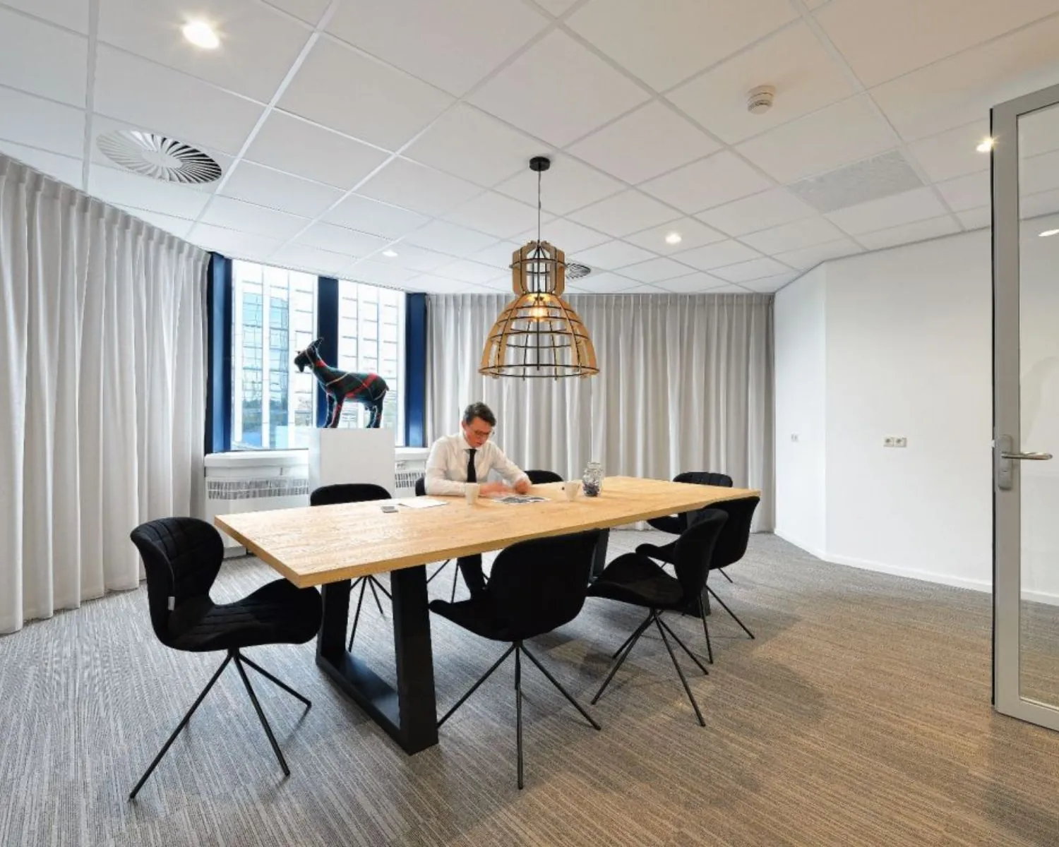 Moderne vergaderruimte in kantoor aan Fellenoord 200-240 in Eindhoven met houten tafel, zwarte stoelen en man aan het werk.