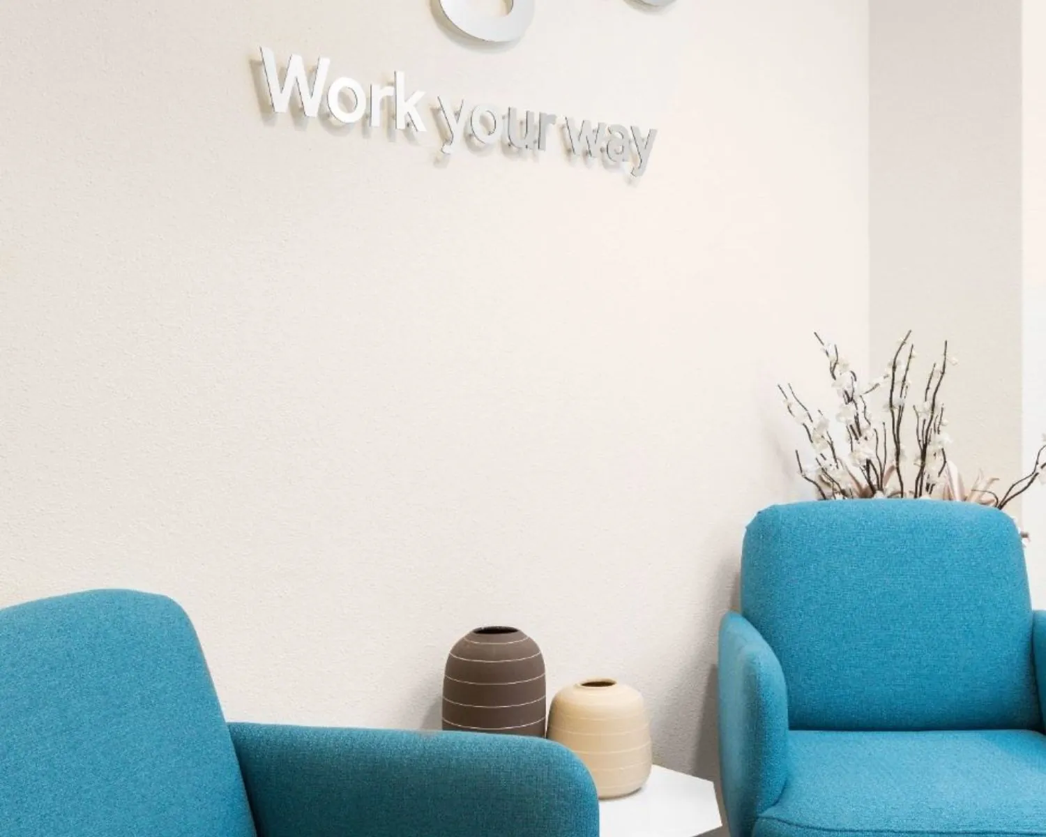 Moderne wachtruimte in kantoor Het Rietveld 55A met blauwe fauteuils, decoratieve vazen en de tekst "Work your way" op de muur.