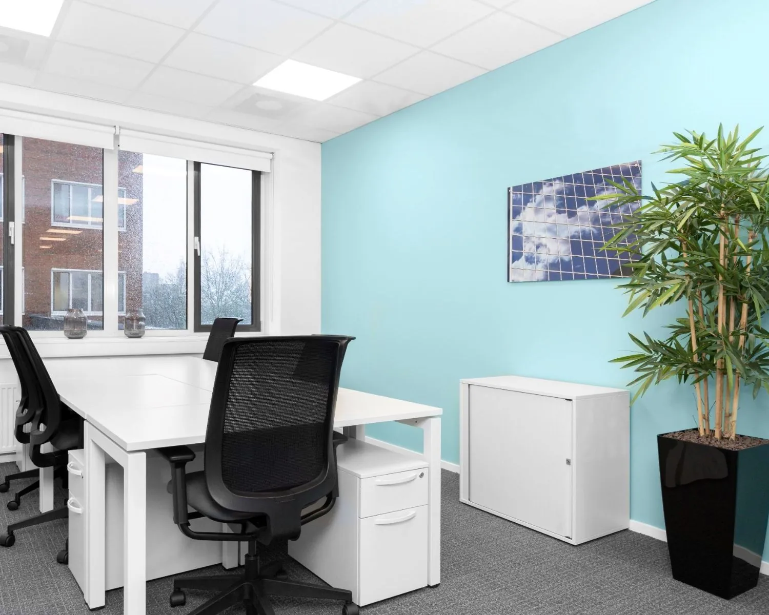 Moderne, lichte kantoorruimte met witte bureaus, zwarte bureaustoelen, een lichtblauwe muur en grote ramen, gelegen op Het Rietveld 55A.