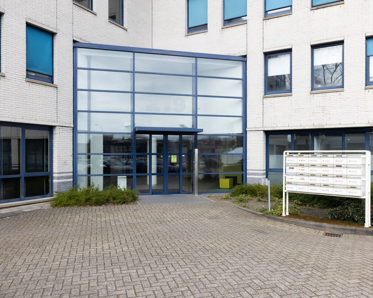 Ingang van een modern kantoorpand aan de Franciscusweg 219 in Hilversum met grote glazen gevel en brievenbussen.