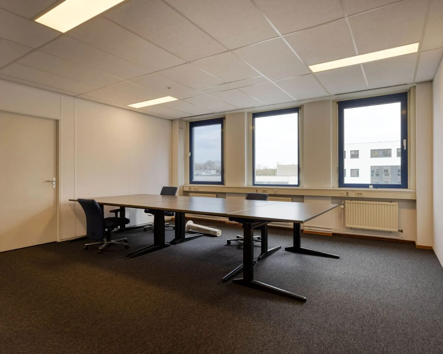 Moderne kantoorruimte aan de Franciscusweg in Hilversum met vergadertafels, bureaustoelen en drie grote ramen.