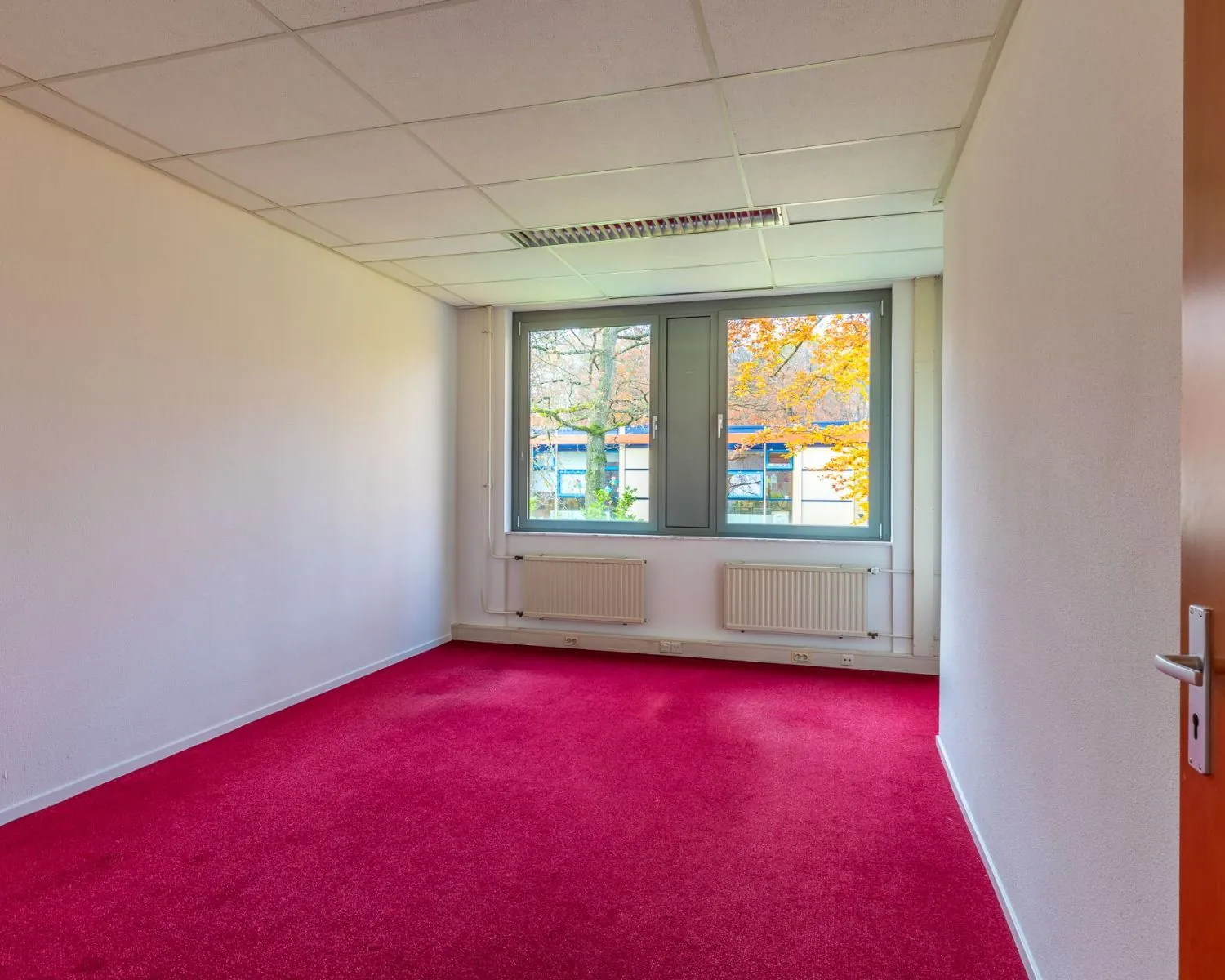 Leeg kantoor met rood tapijt en grote ramen aan de Mozartlaan 27 in Hilversum.