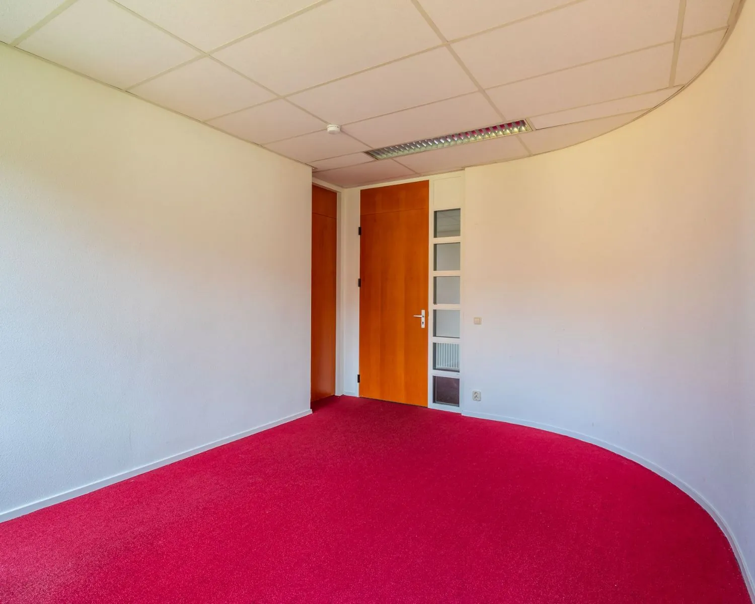 Leeg kantoor met rode vloerbedekking en houten deur in Hilversum aan de Mozartlaan 27.