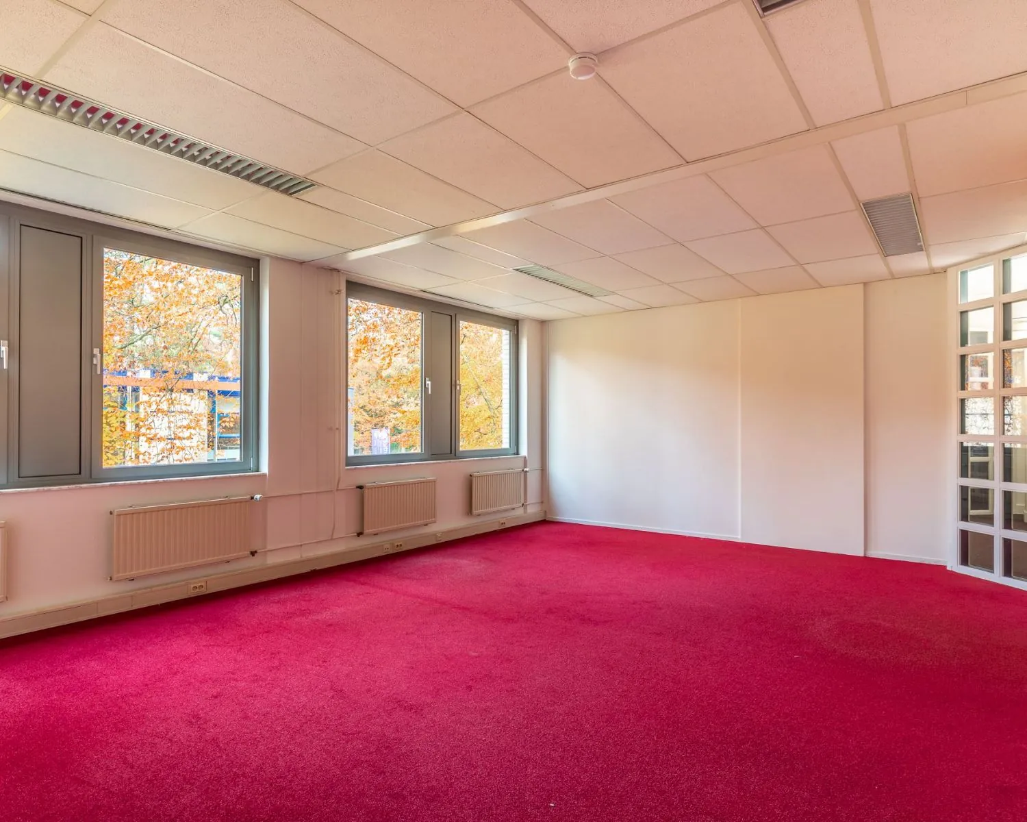 Lichte kantoorruimte aan de Mozartlaan 27 in Hilversum met rood tapijt en grote ramen.