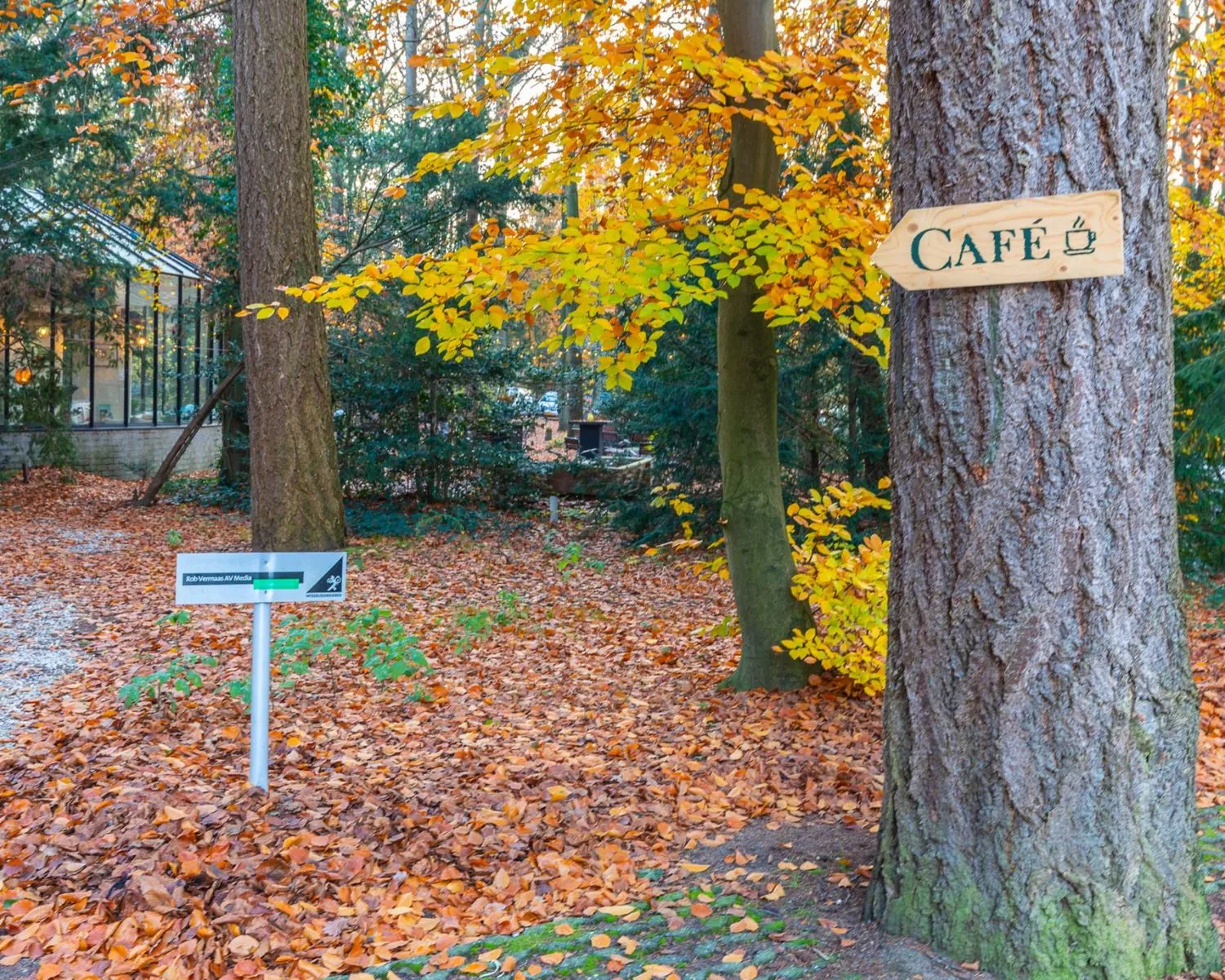 Pad in een bosrijke omgeving bij Mozartlaan 27 in Hilversum met een bord naar een café en een wegwijzer naar kantoorruimte.